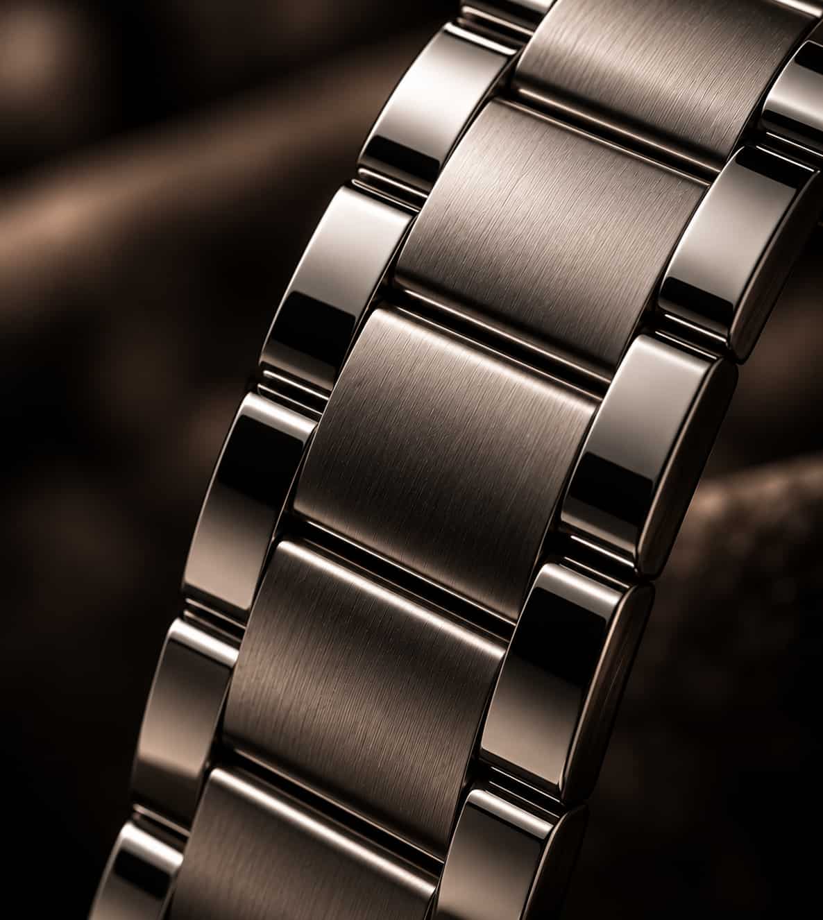 Close-up of a brushed stainless steel watch band with polished links, shown against a dark brown background.
