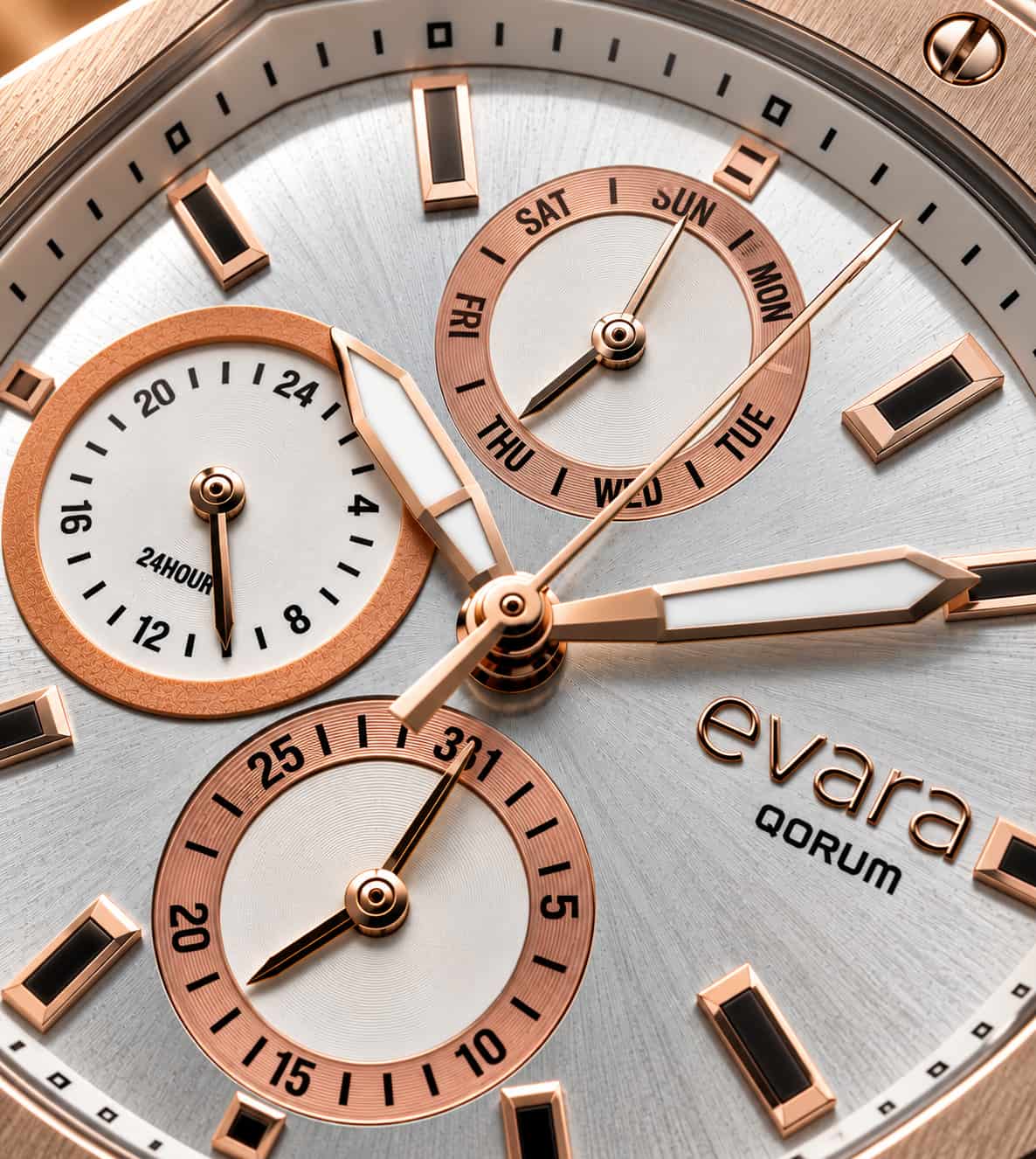 Close-up of an Evara Qorum watch dial with a silver-toned textured background, rose gold bezel and subdials, white hands and markers, and black hour indices.