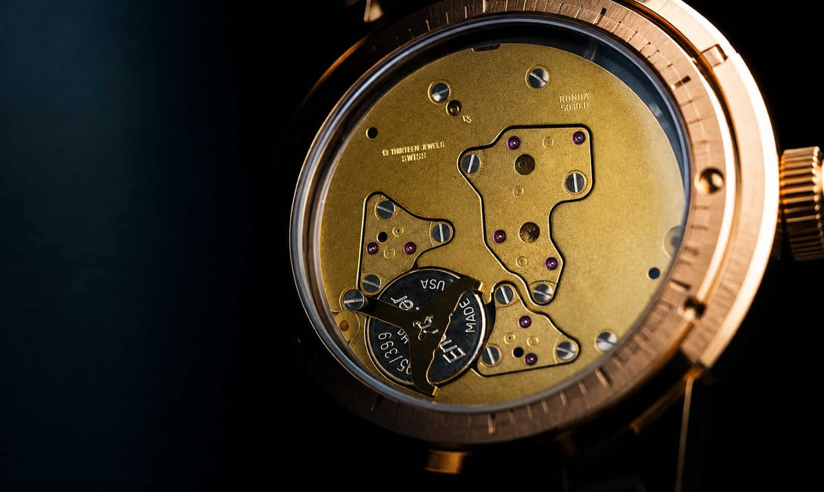 Close-up of a luxury watch showing the intricate gold-toned mechanical movement and internal components through a transparent case against a dark background.