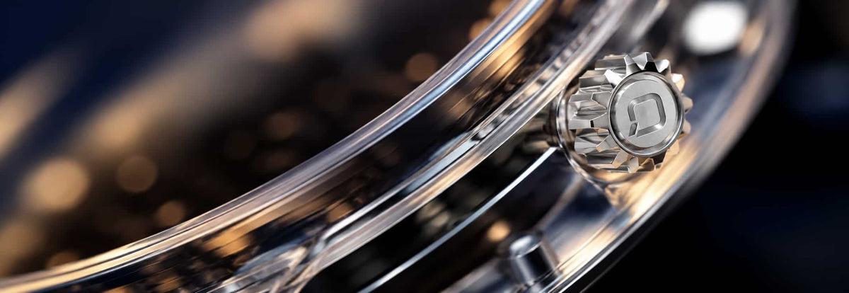 Close-up of a shiny metallic drum shell with a visible drum head attachment and reflective chrome finish against a dark blurred background.