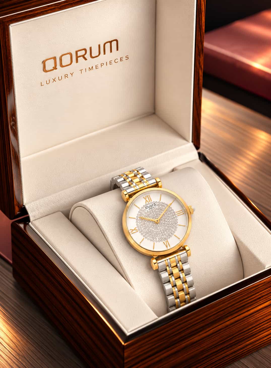 A luxury watch by QORUM, featuring a gold and silver two-tone stainless steel bracelet, a gold case, and a white dial with a crystal-embellished center, presented inside its open wooden box.
