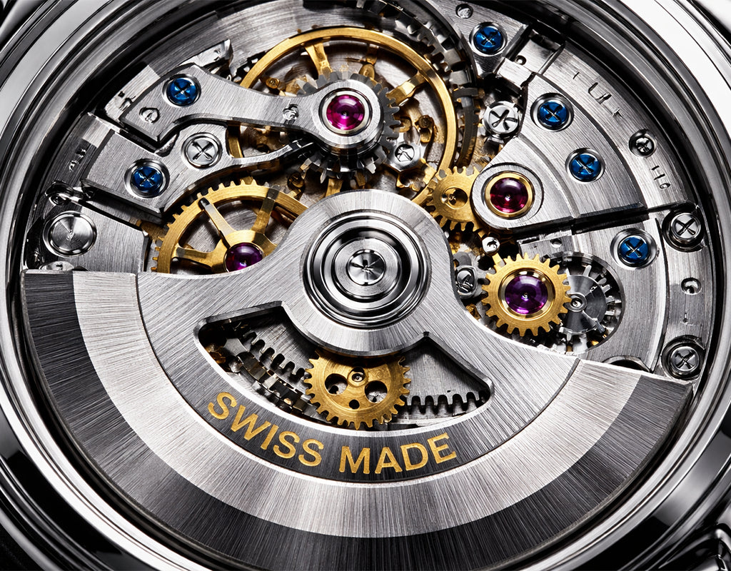 Close-up of a Swiss-made automatic watch movement with visible gears, screws, jewel bearings, and a brushed metal case. Gold-toned gears and a silver-toned outer ring are prominent, with small purple and blue jewel accents and the words "SWISS MADE" engraved on the lower ring.