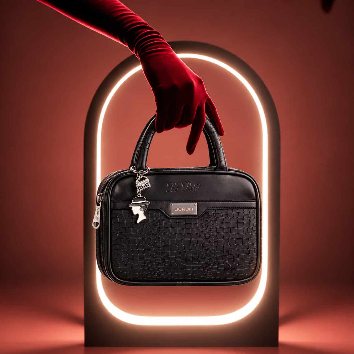 A black textured leather handbag with silver hardware and a small front plaque reading GORUSH, held by a red-gloved hand in front of a glowing arch on a warm red background.